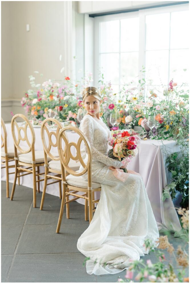 bride holds colorful wedding bouquet sitting at table decorated in florals