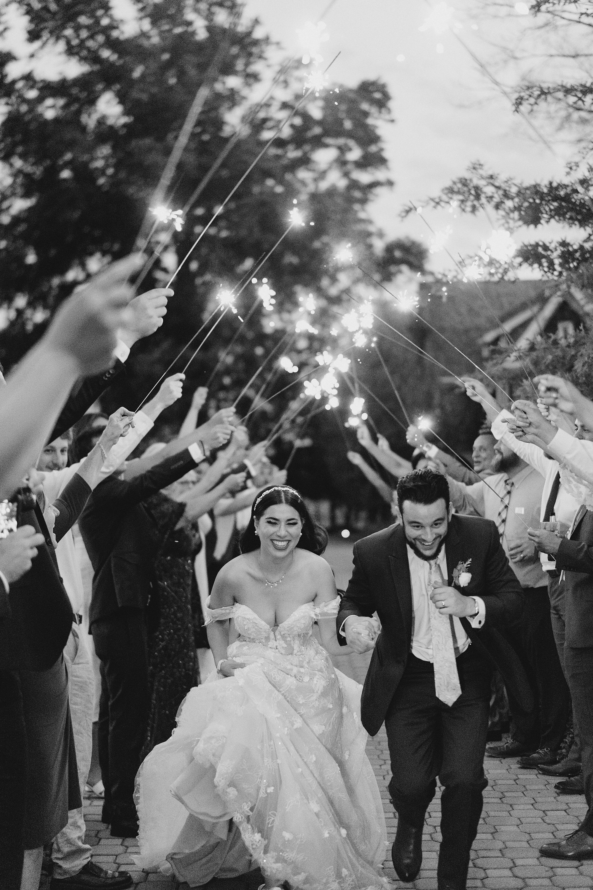 wedding guests hold sparklers up to make a tunnel as newlyweds exit reception