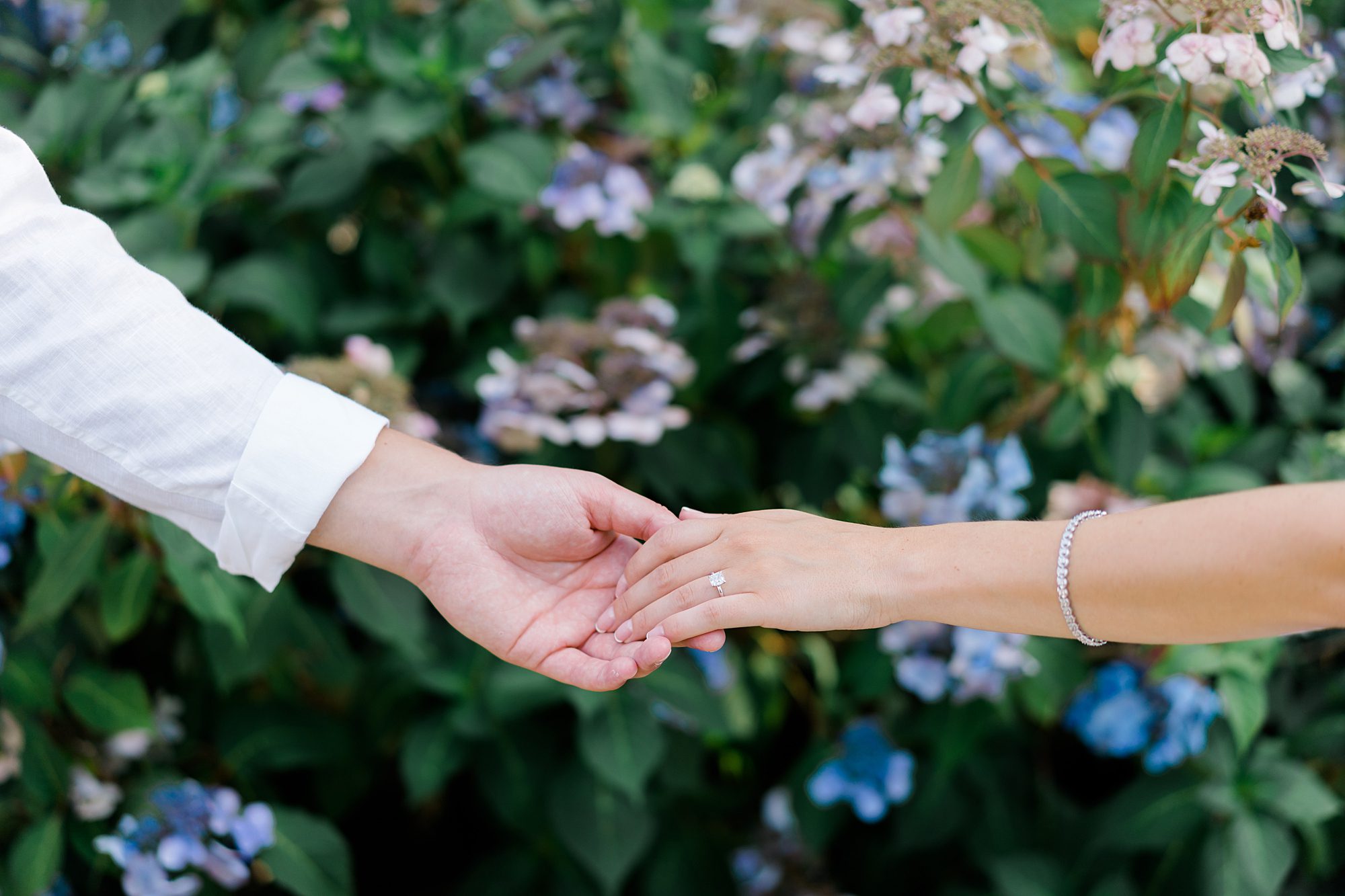 couples holding hands in front of flowers at an estate during engagement photos