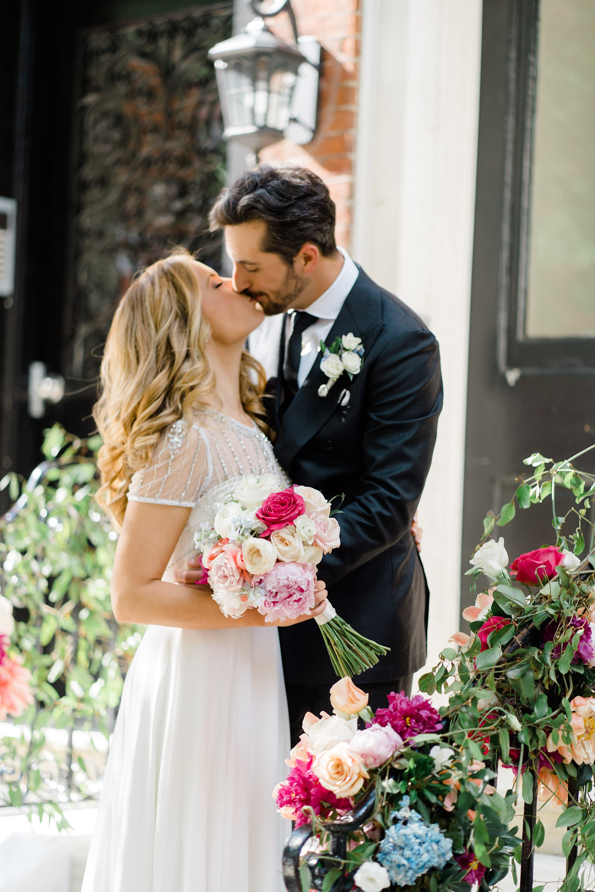 bride and groom kiss surrounded by beautiful wedding flowers outside wedding venue