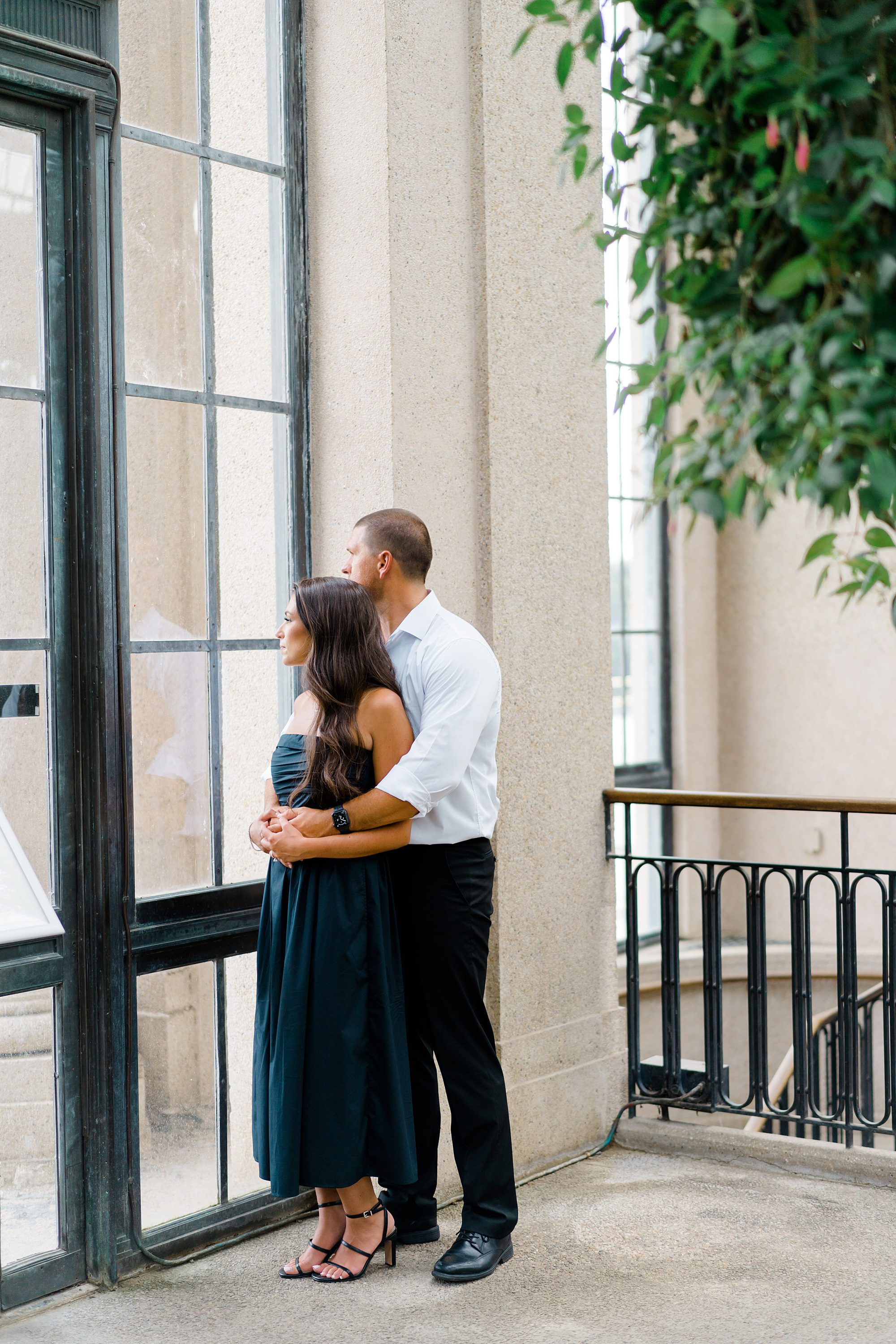 couple hold each other and look out window during Timeless Longwood Gardens Engagement portraits
