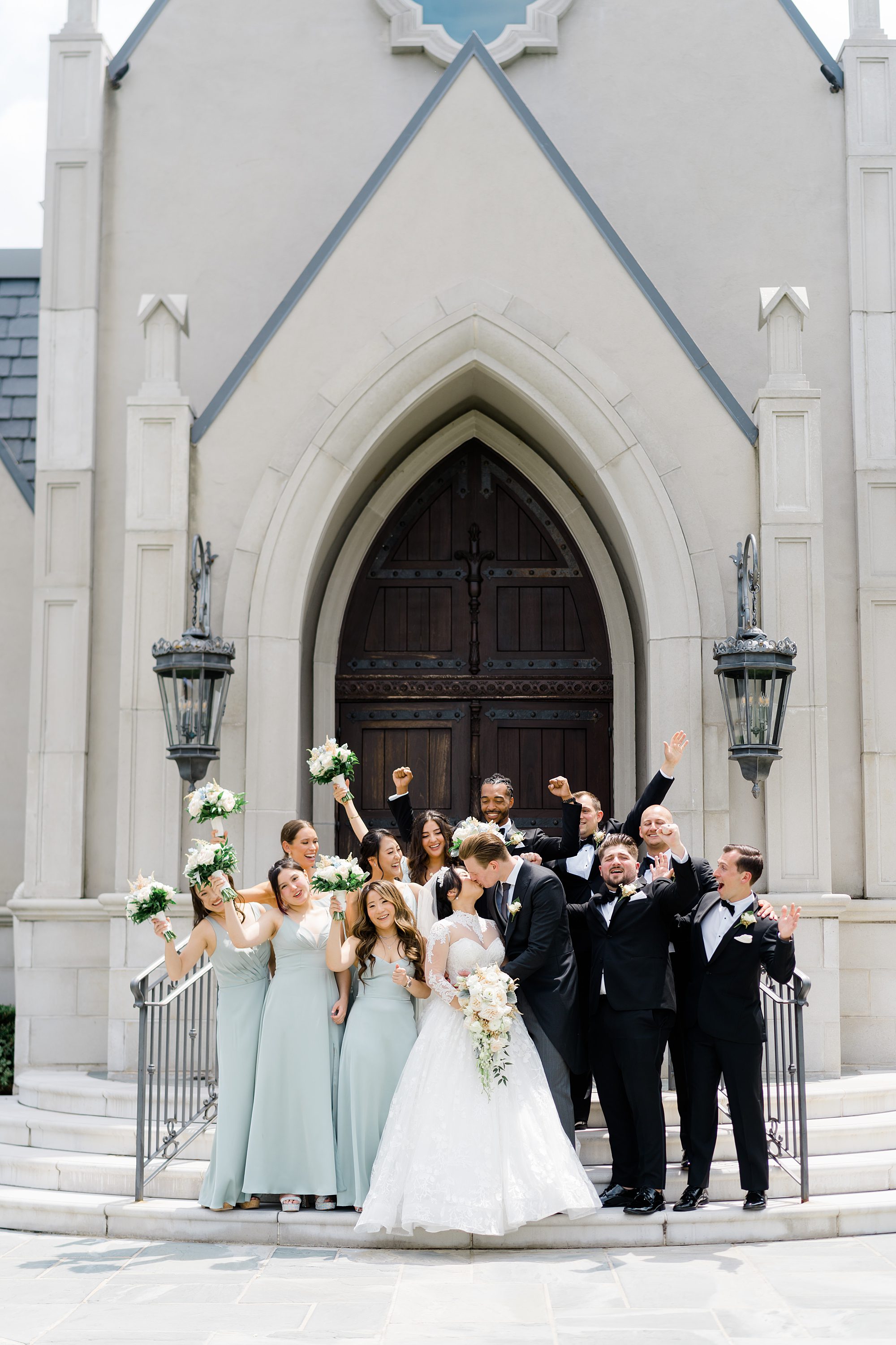 bridal party stands on steps of chapel after wedding ceremony