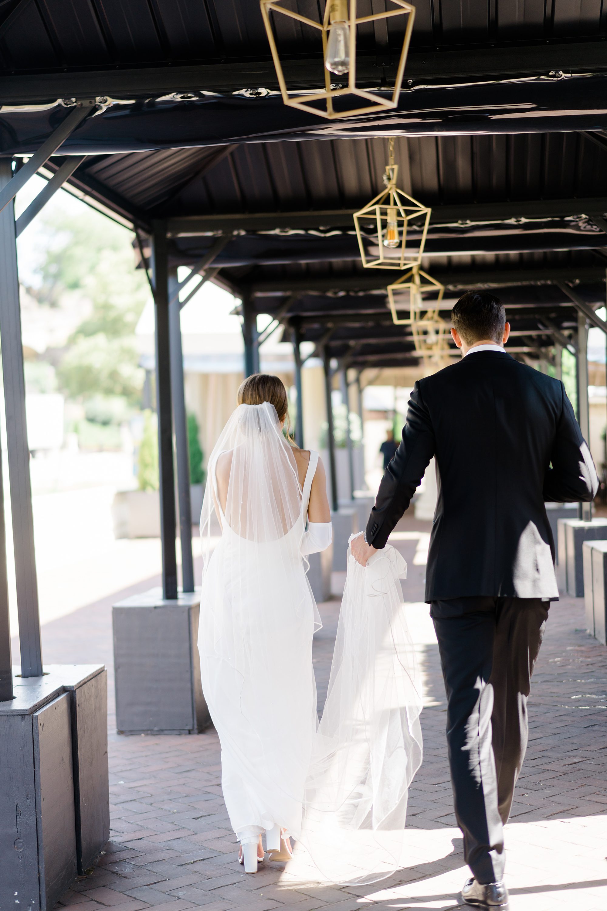 groom holds bride's wedding dress as they walk together