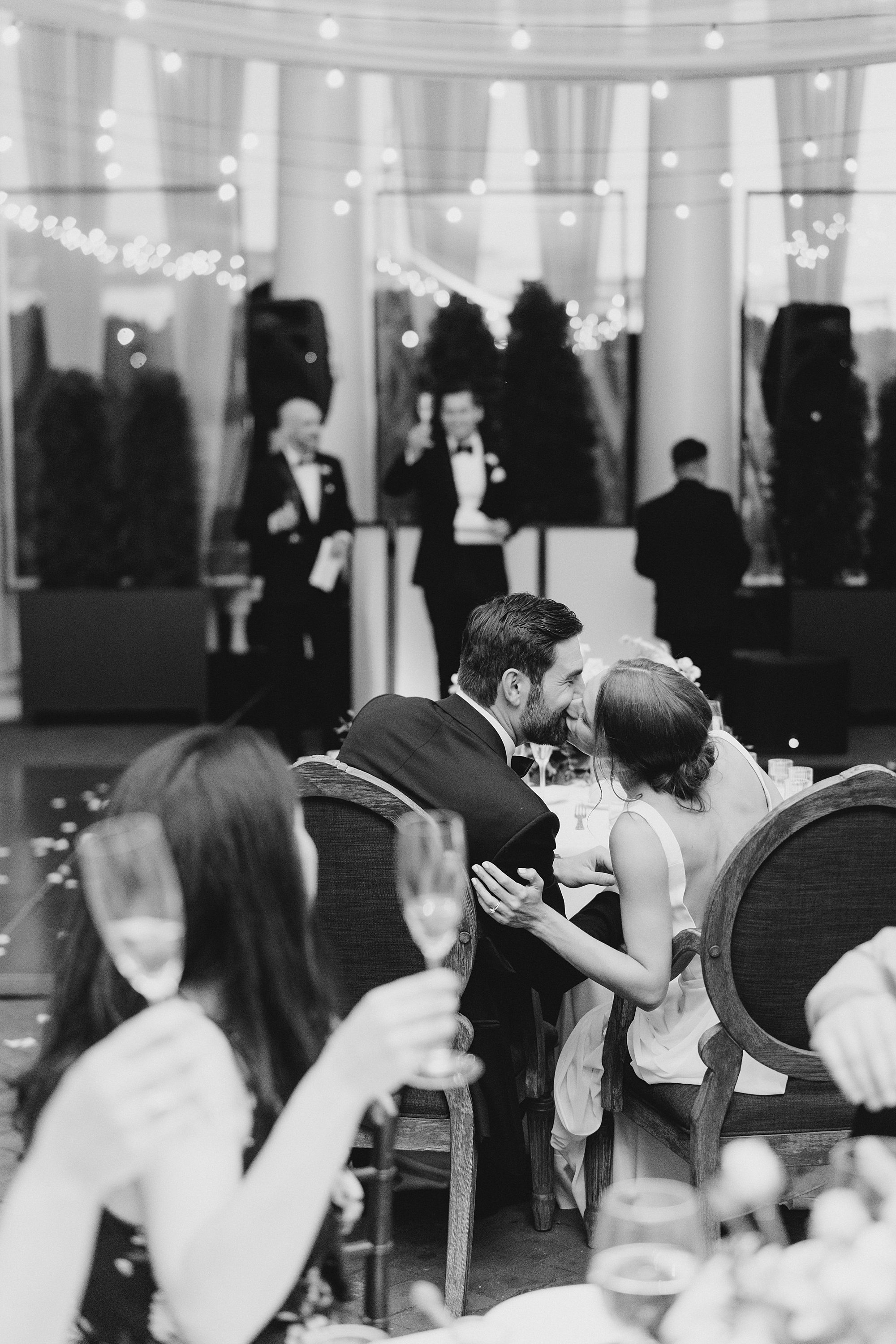 couple steal a kiss as the sit together at reception