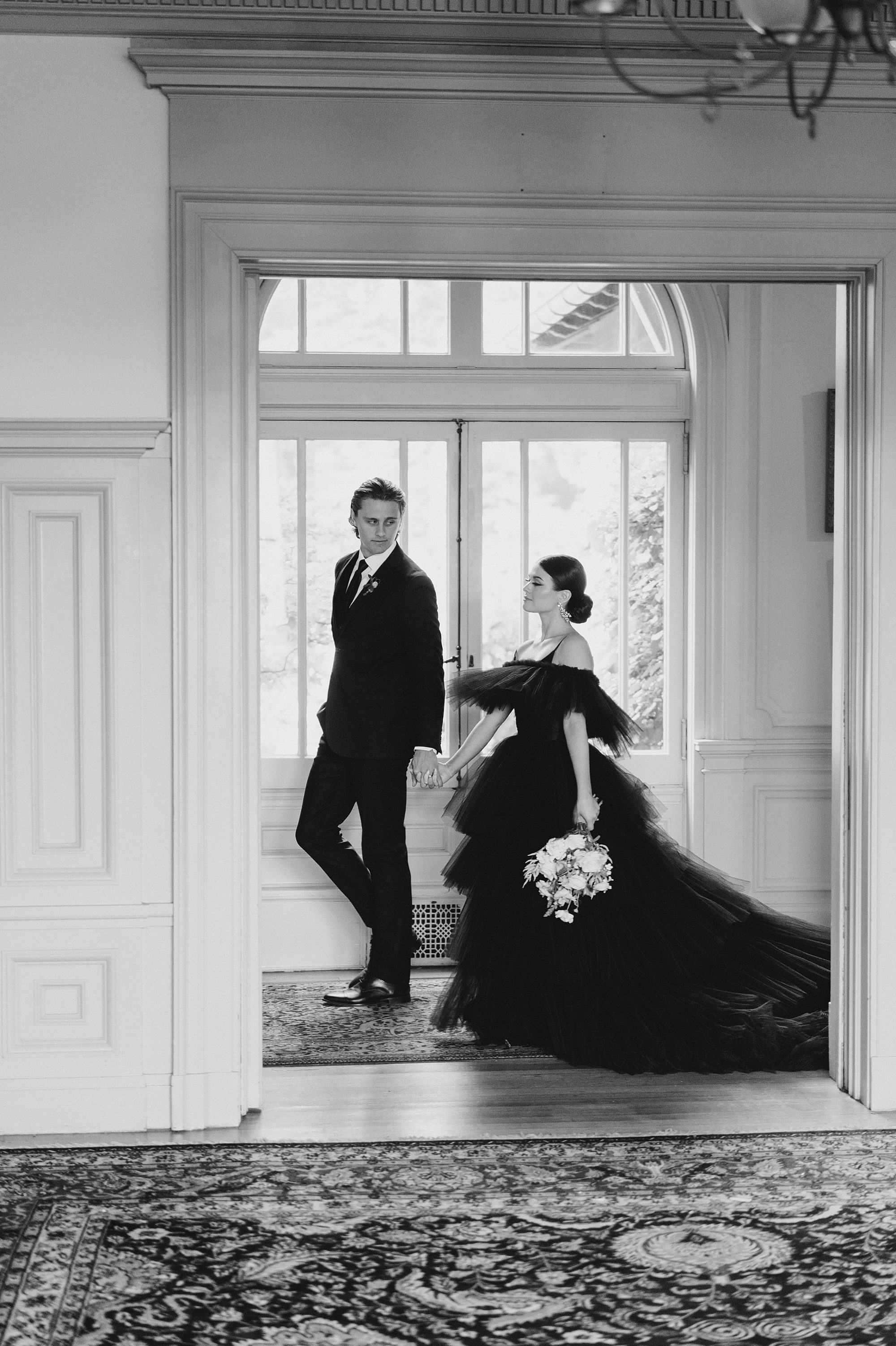 couple in modern black wedding attire walk through Cairnwood Estate in PA