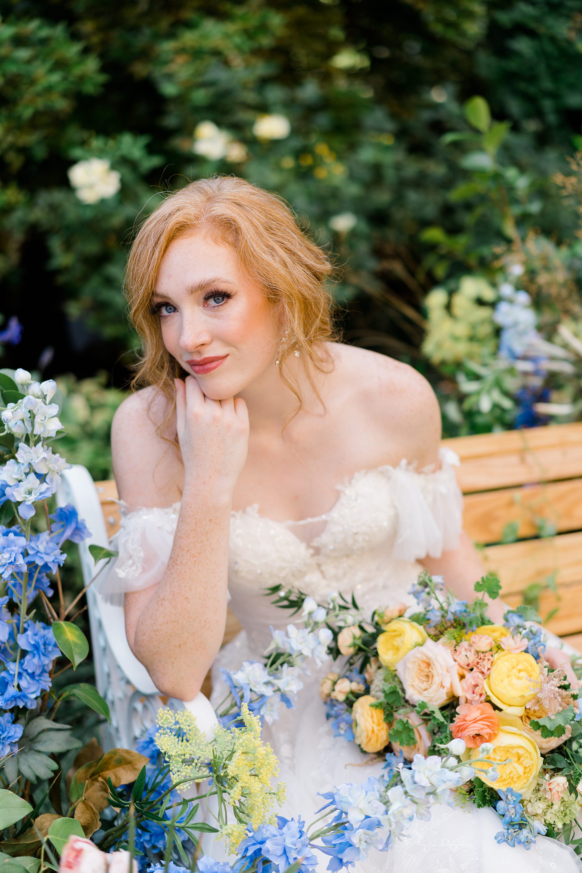 bride sits on bench surrounded by flowers