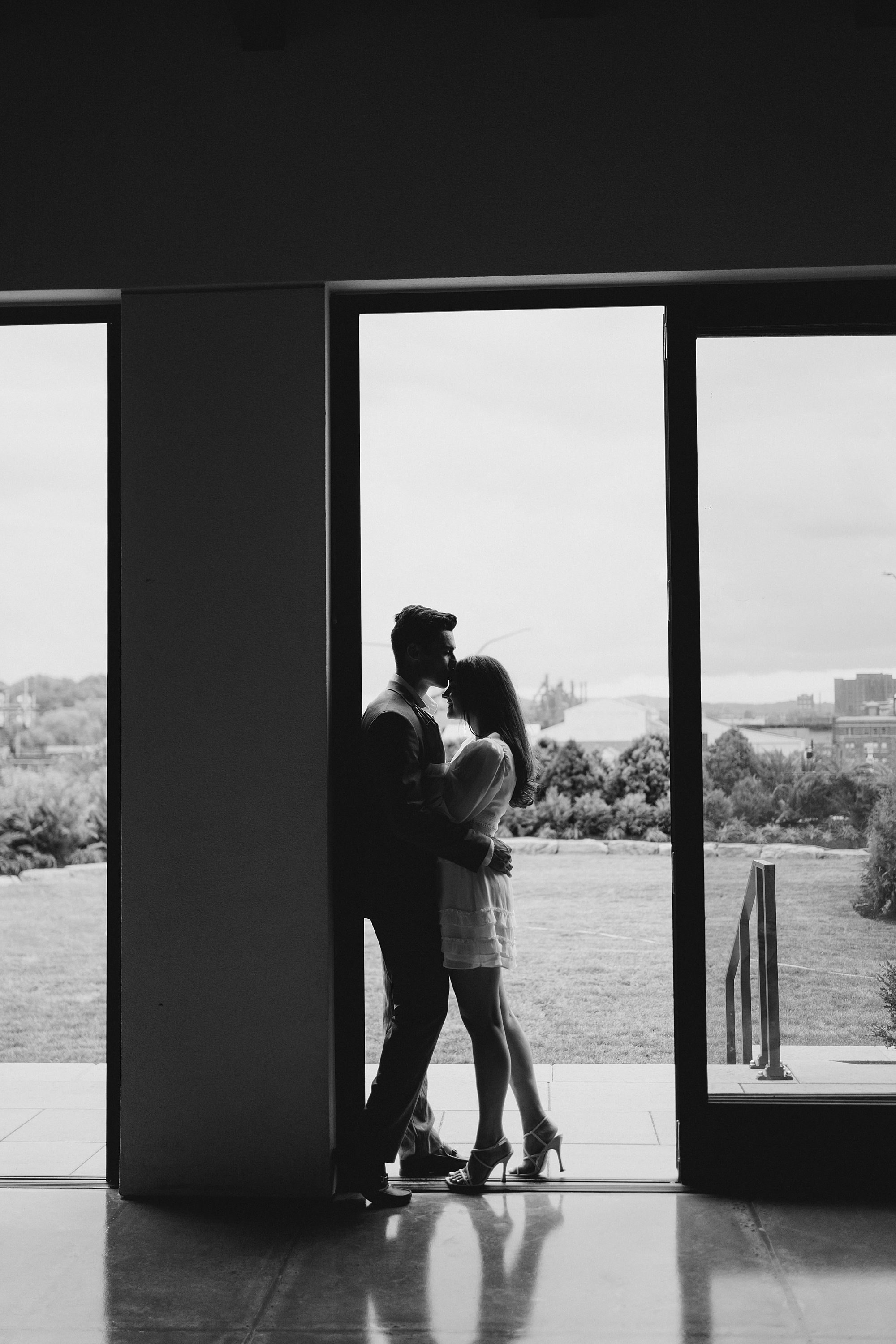 couple kiss near patio doors to balcony of mansion