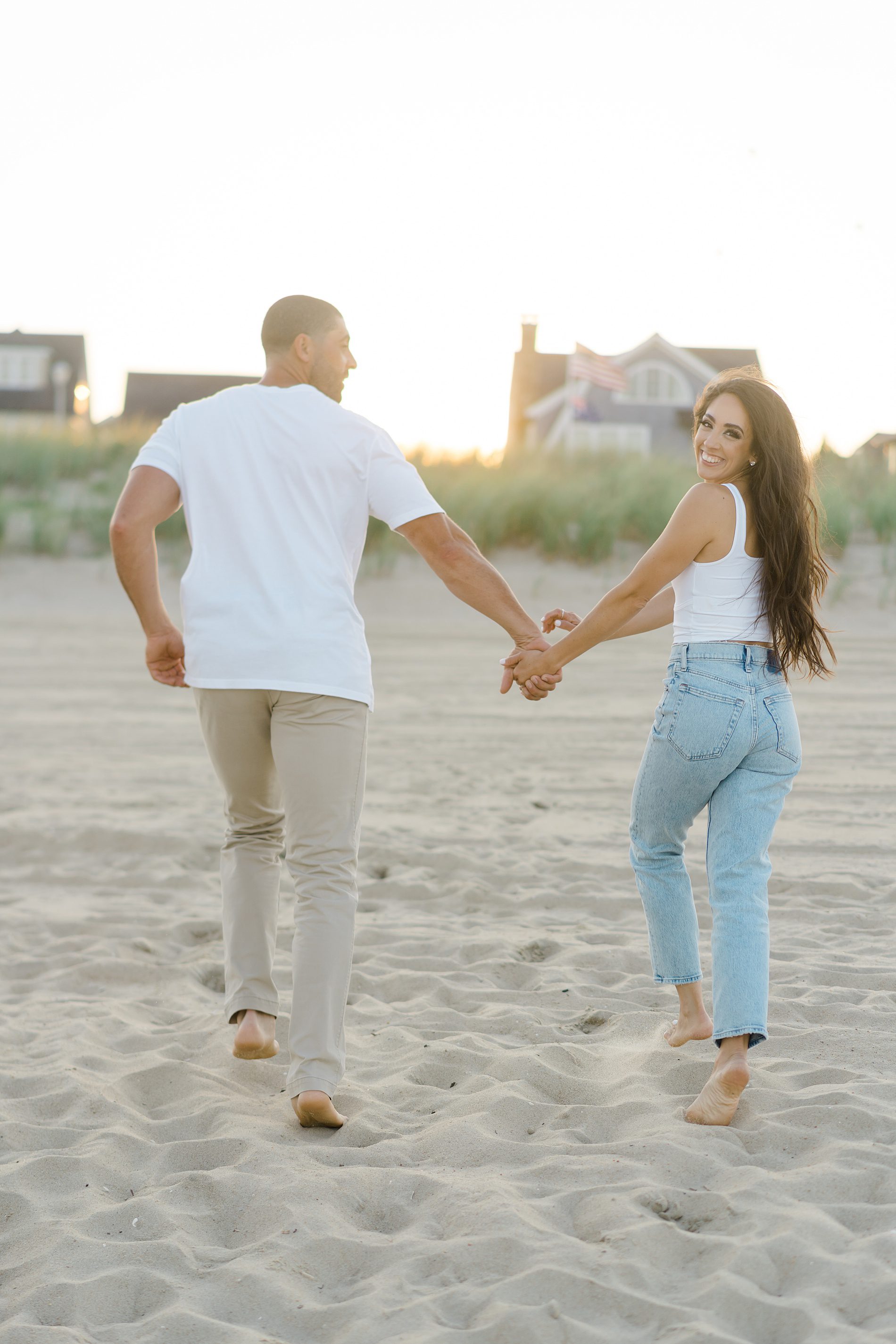 couple hold hands and run up the beach looking back