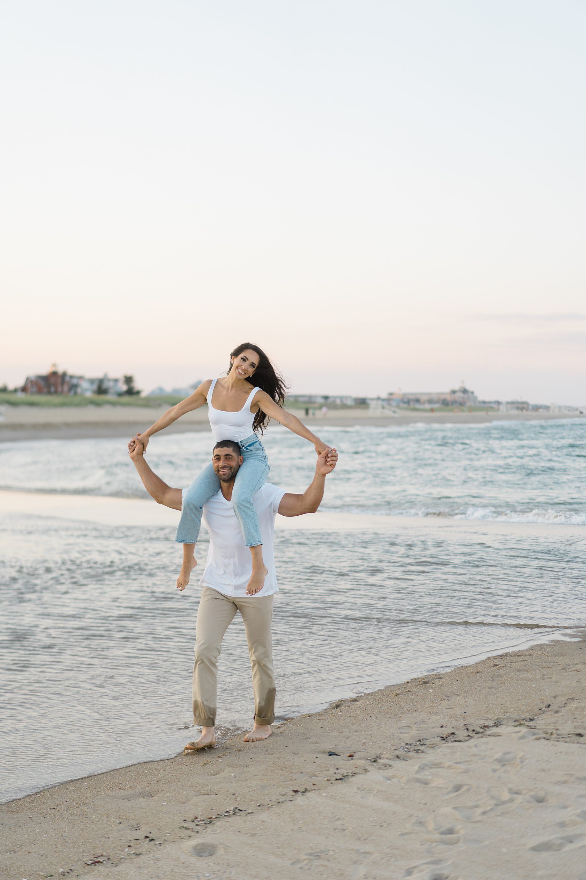 man carries his fiance on his shoulders at the beach