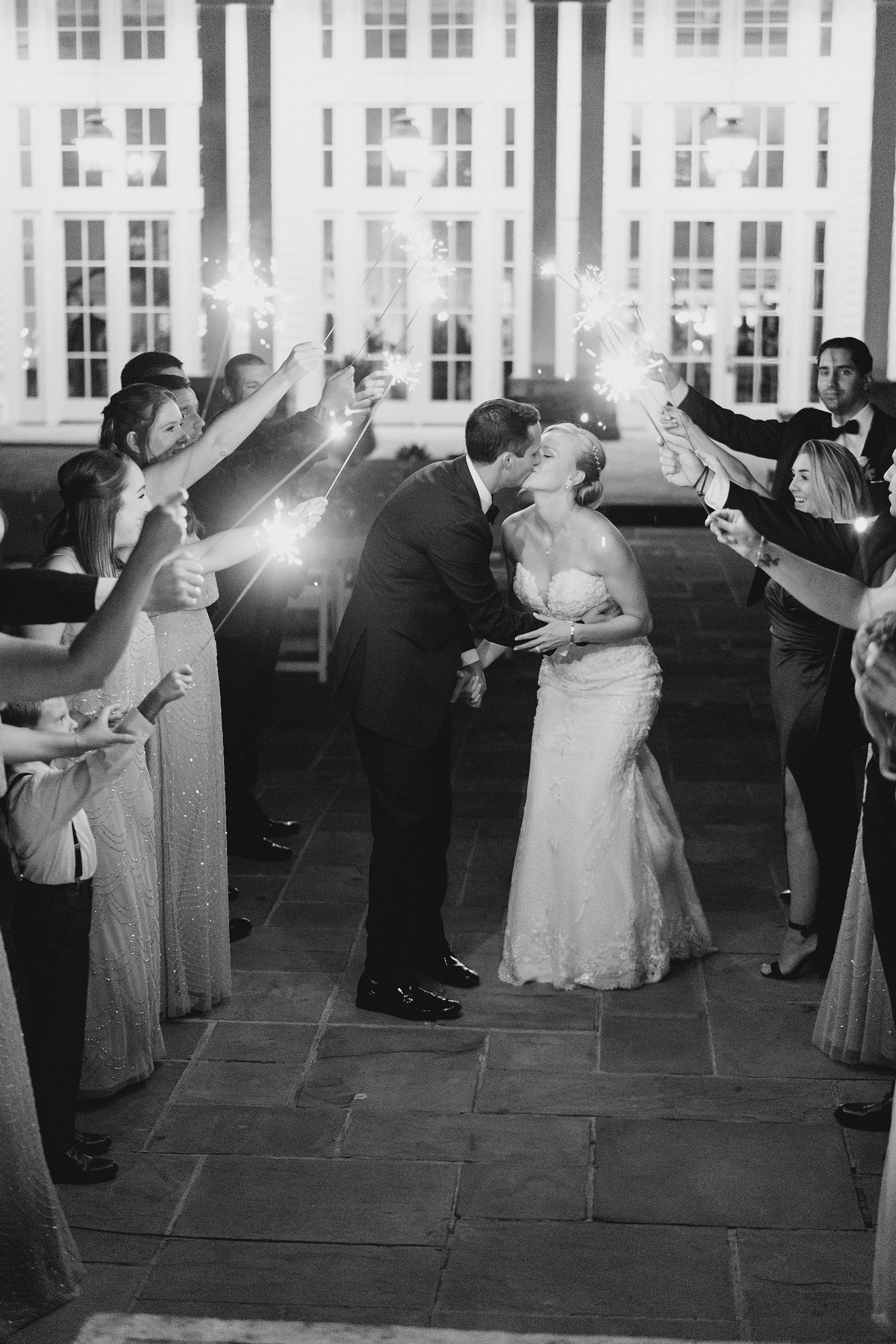 couple kiss as guests hold up sparklers during wedding exit