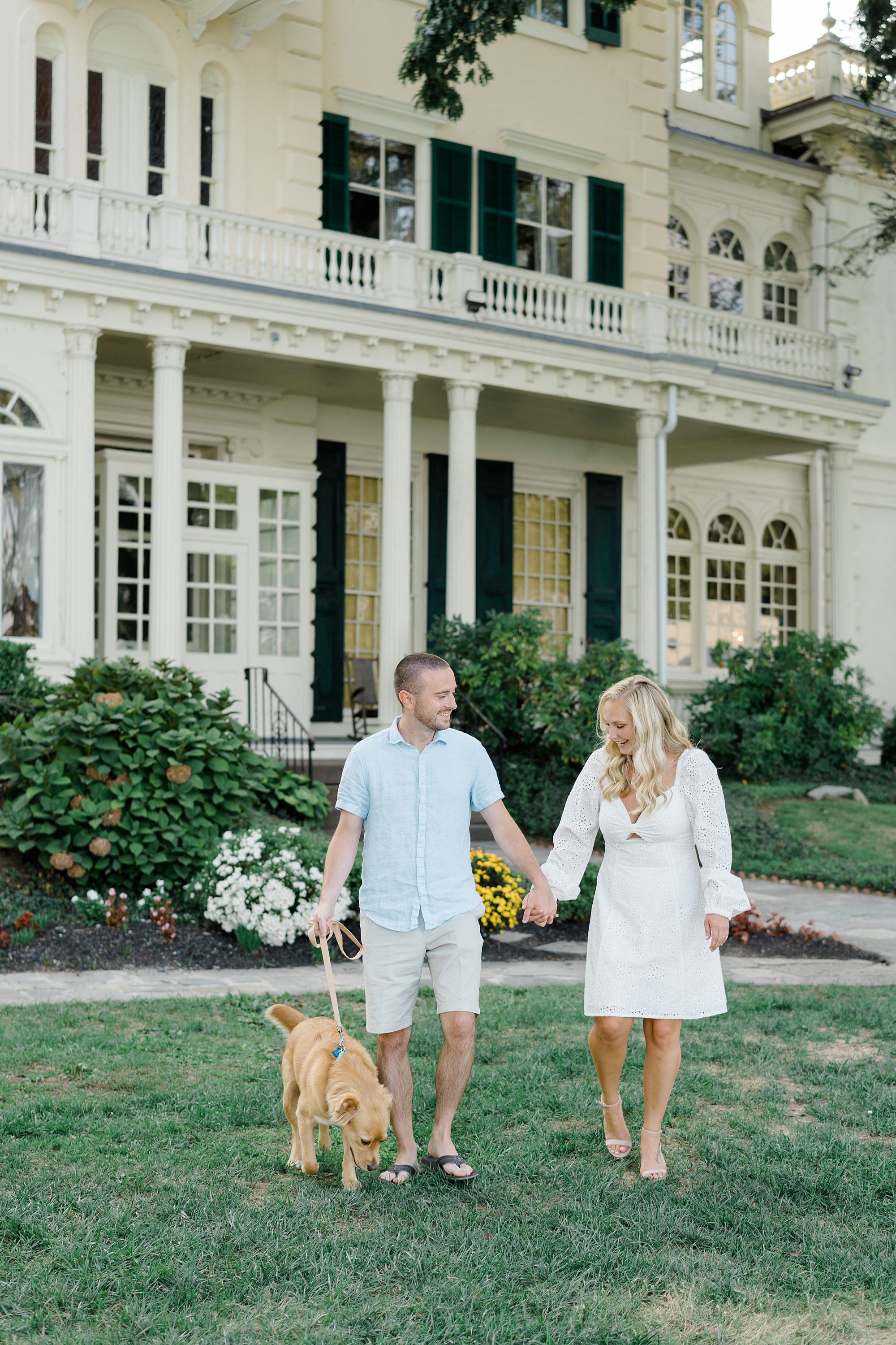 engaged couple walk their dog while holding hands