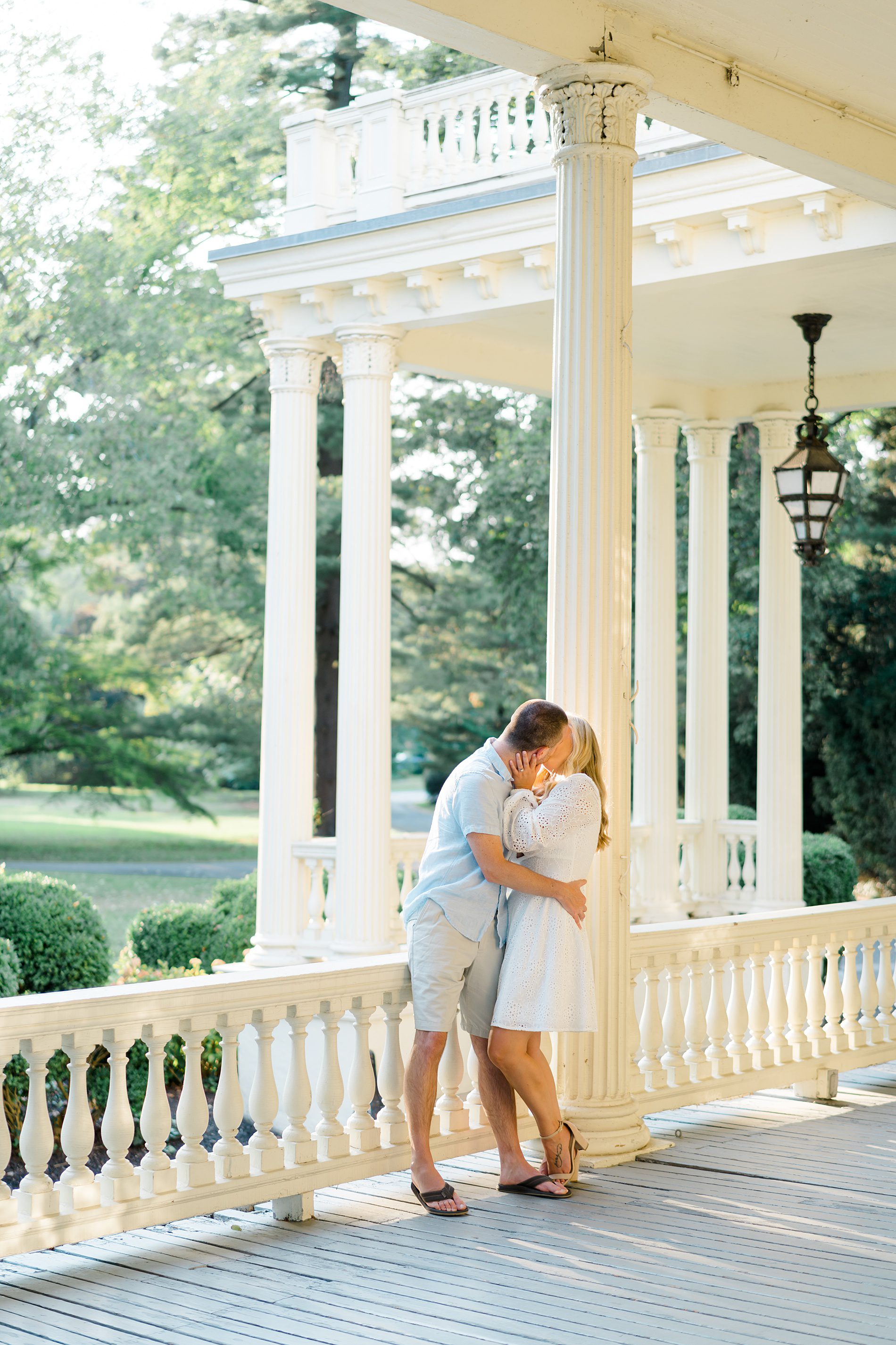 Engaged couple kiss on the porch of Philadelphia wedding venue