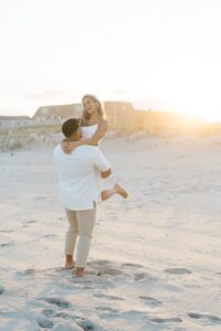 man lifts his fiancé up on the sandy beach of NJ