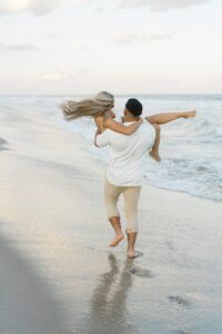 man carries his fiancé on the beach