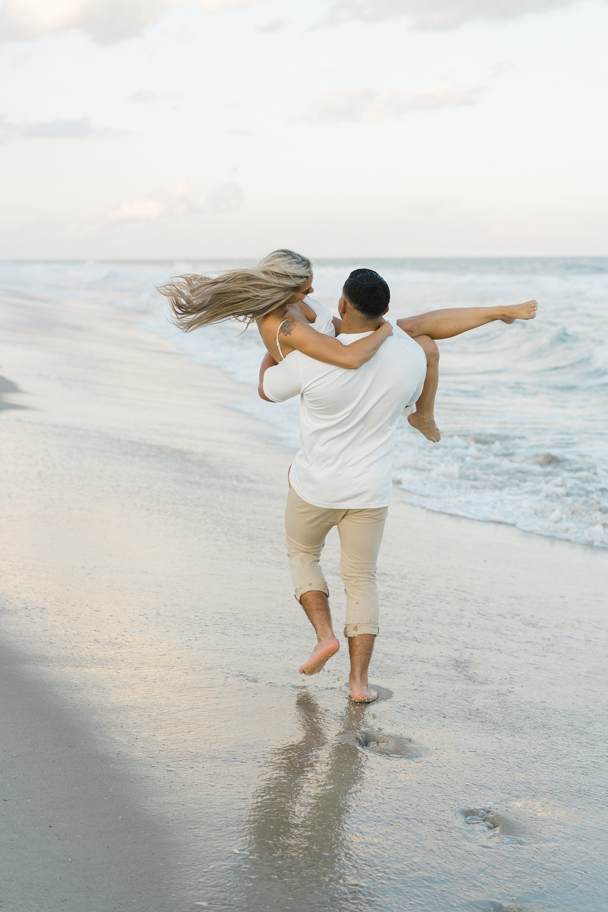 man carries his fiancé on the beach