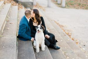 couple kiss on stairs with dog during engagement session