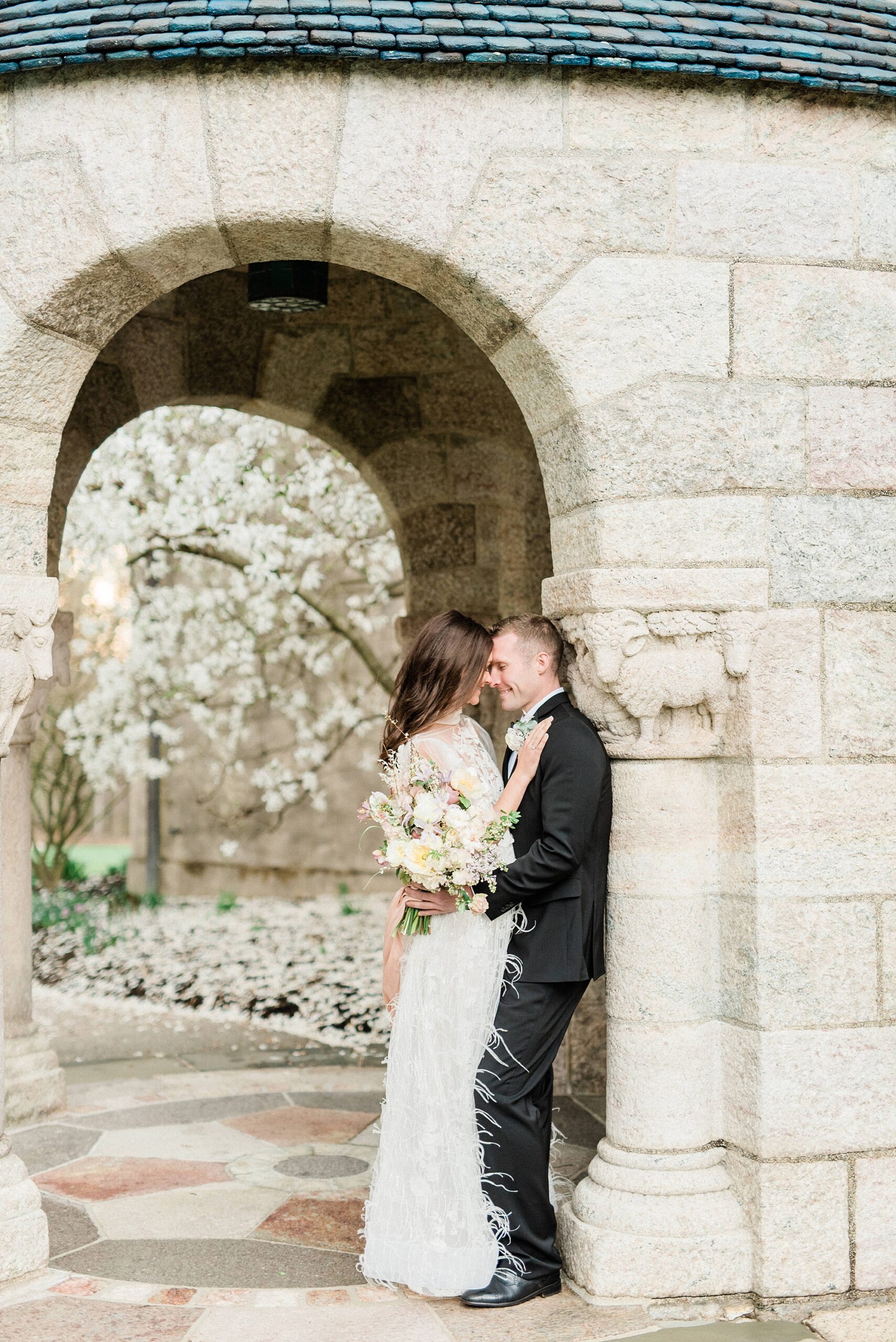 bride and groom lean up against stone archway in the courtyard of Cairnwood Estate