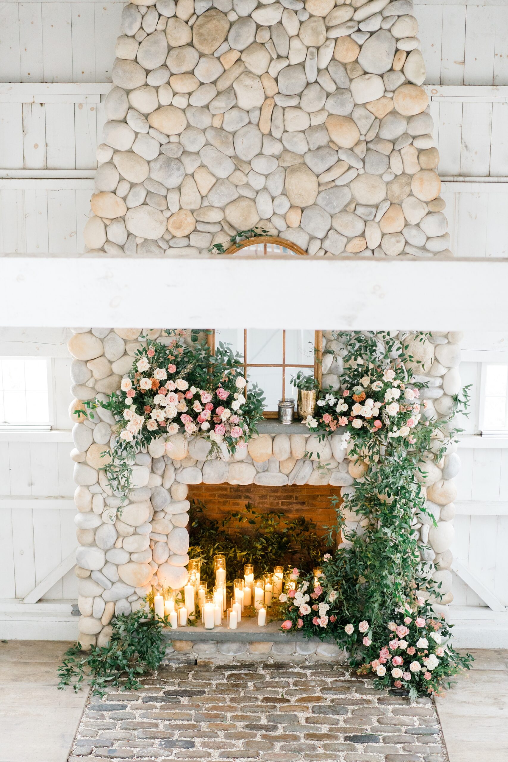 stunning stone fireplace decorated in lush greenery and pink and white flowers