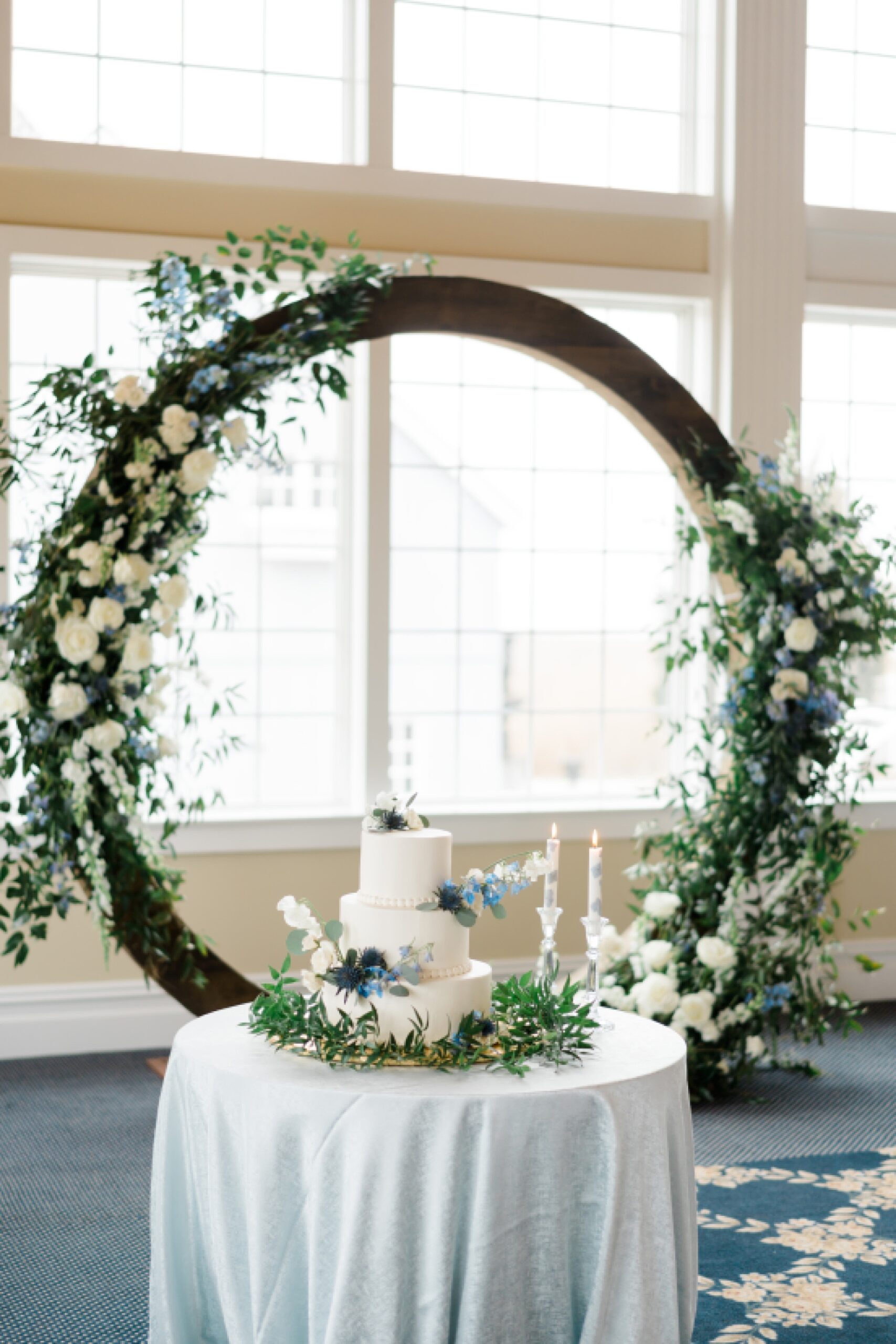 wooden wedding arch decorated with florals and greenery behind cake table