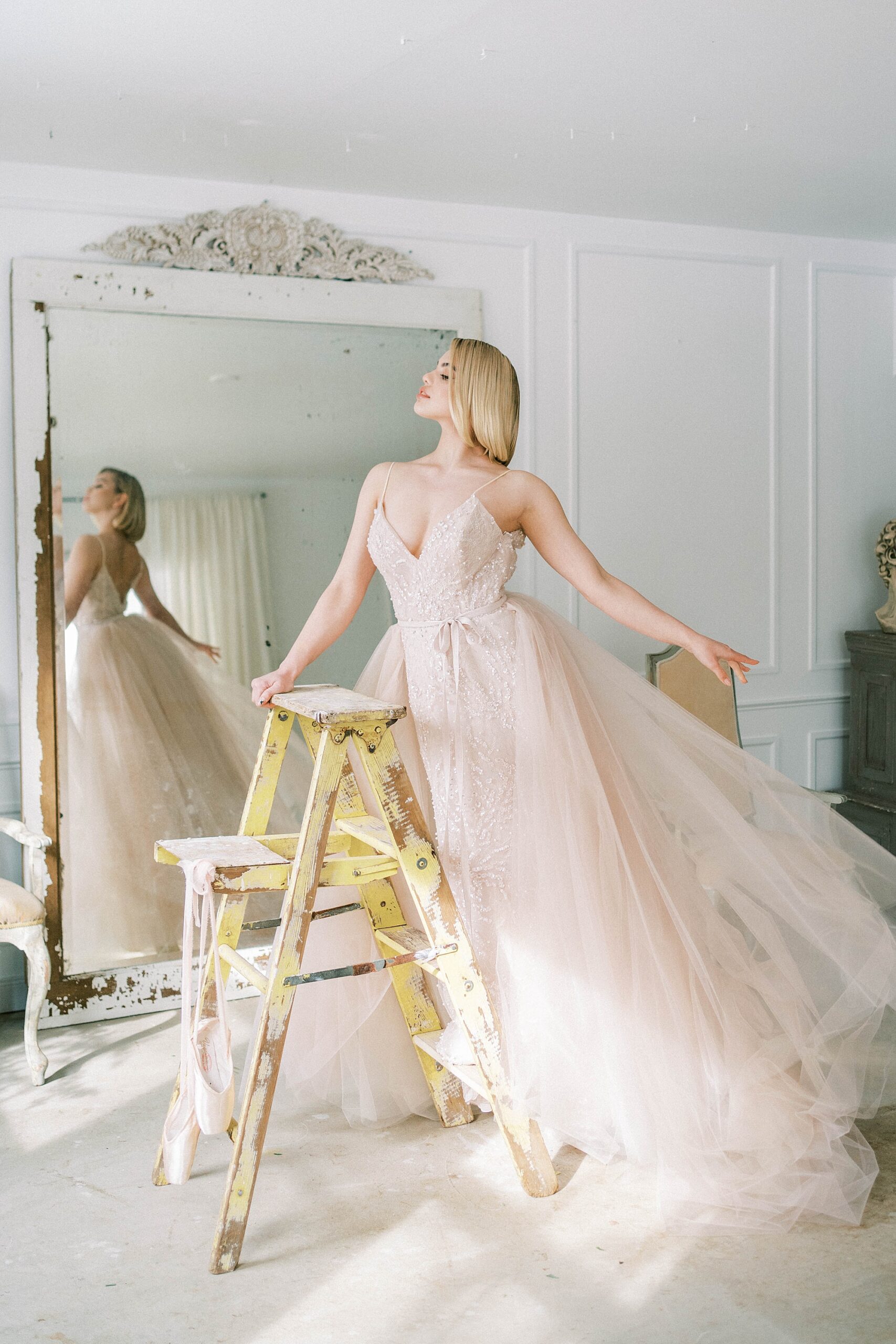bride poses on ladder showing off tulle on wedding dress 