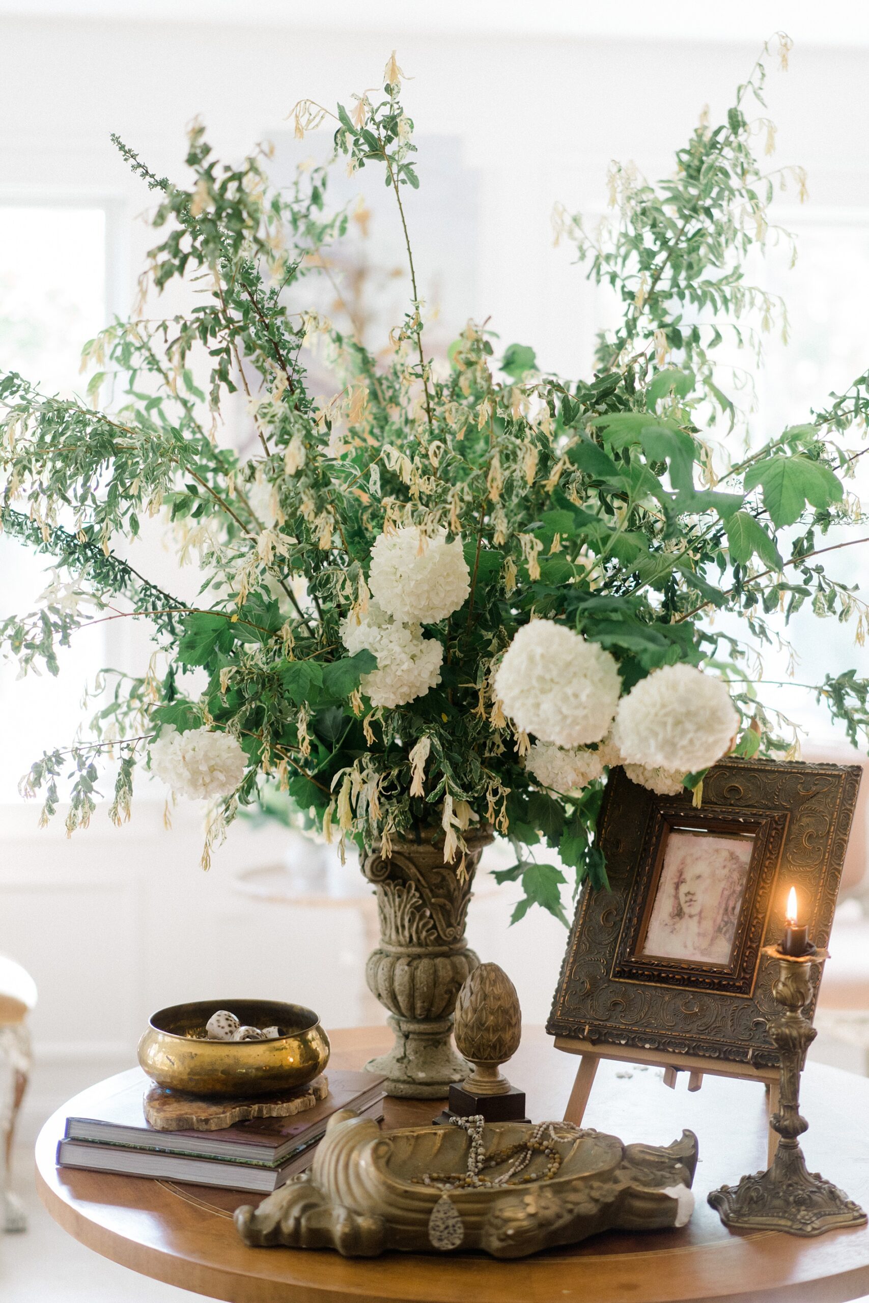 white flowers with vibrant greenery in vintage vase surrounded by artifacts
