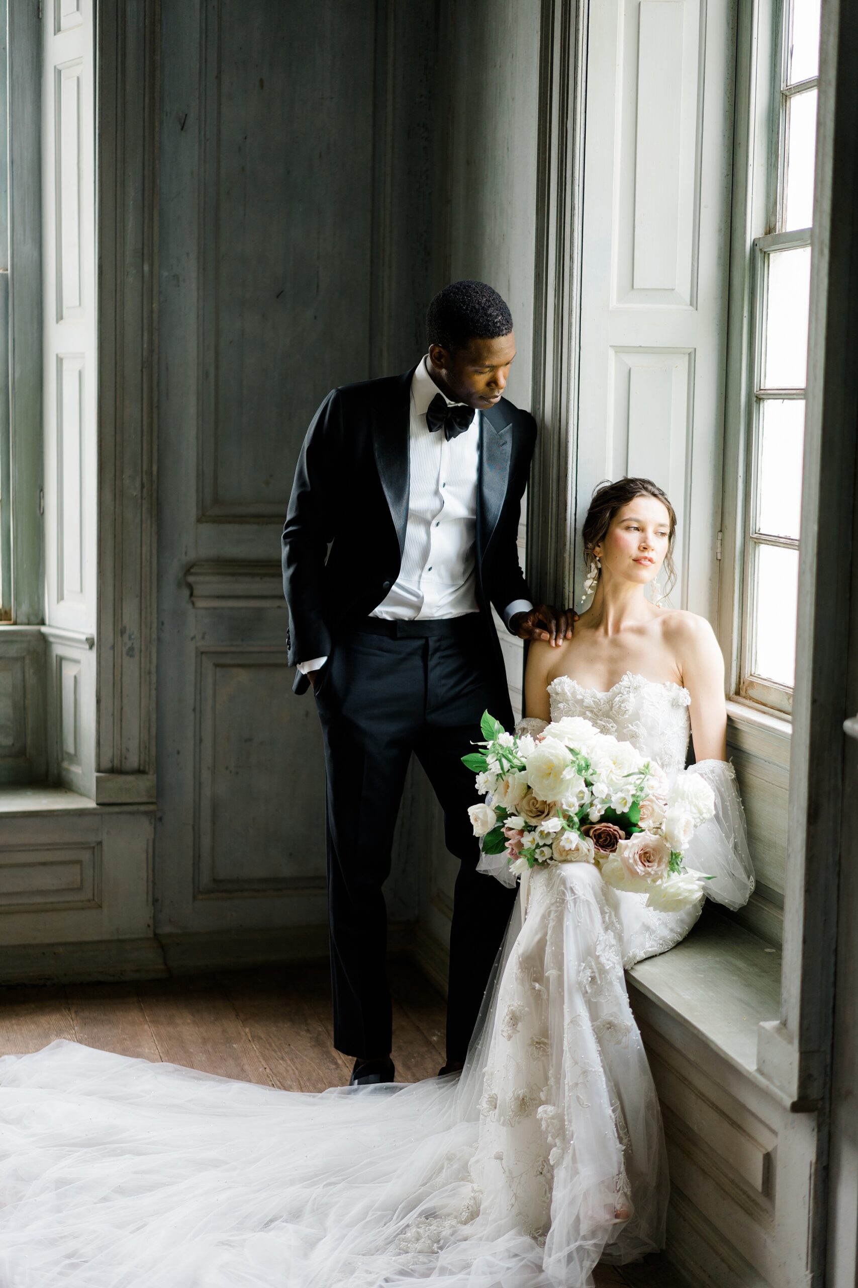 bride and groom stand by window