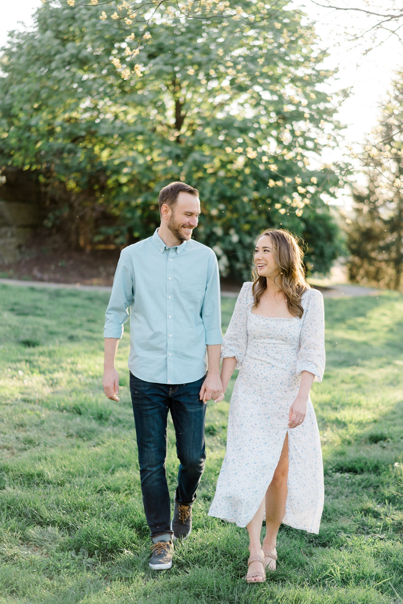 Light + Airy Philadelphia Engagement of couple holding hands as they walk through field 