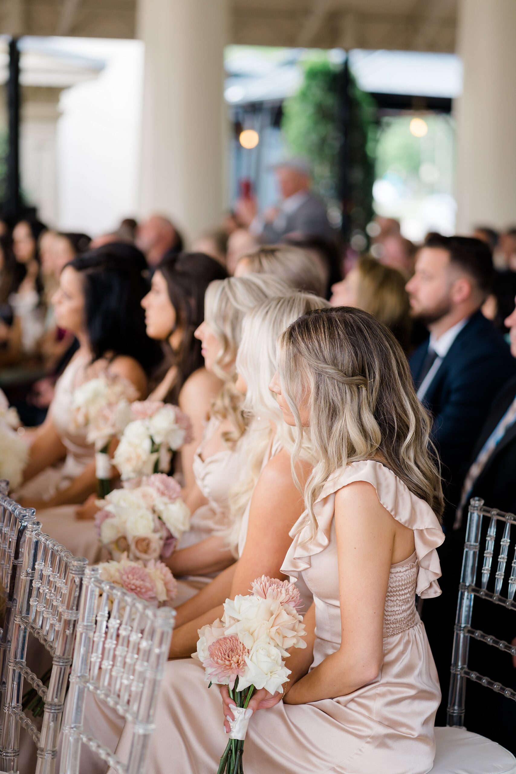 bridesmaids in champagne colored dresses listen at wedding ceremony 