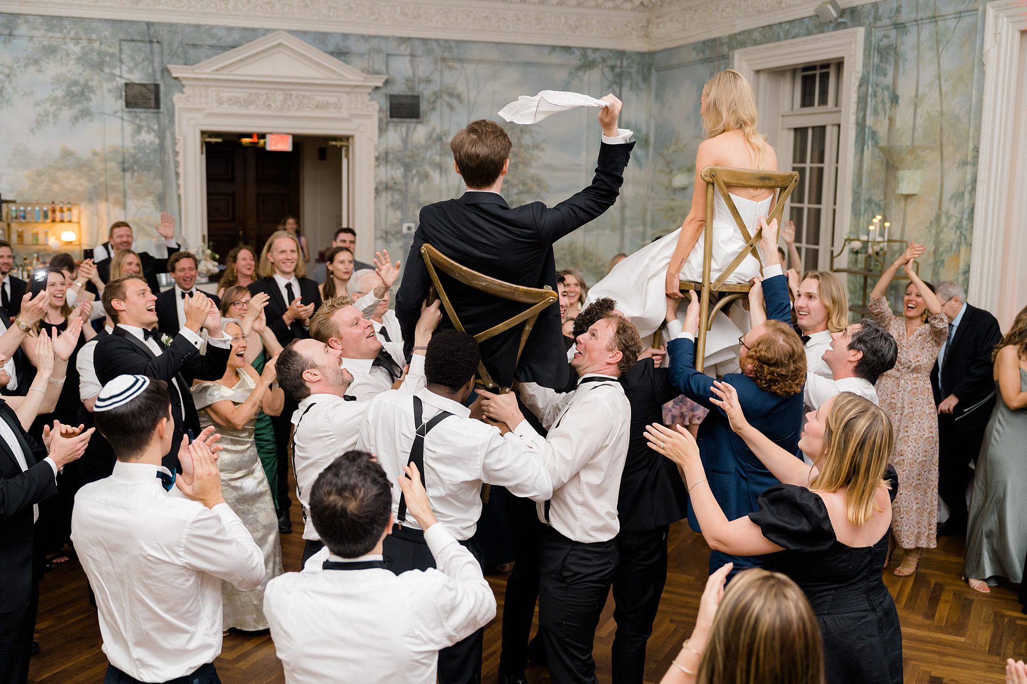 bride and groom are lifted up onto chairs during wedding reception