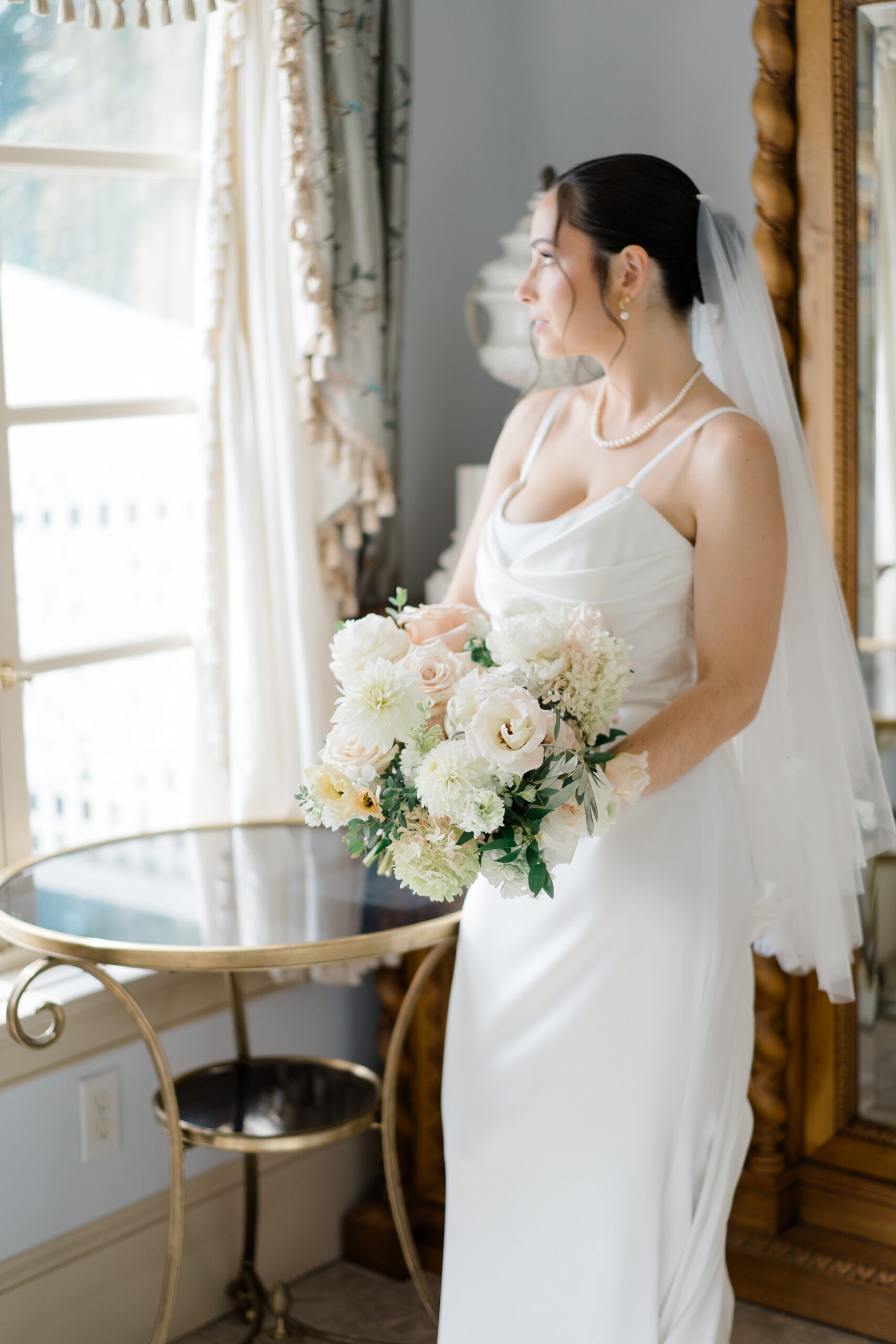 bride looks out window of room as she gets ready from Romantic Floral-Centered Wedding at The Inn at Barley Sheaf Farm