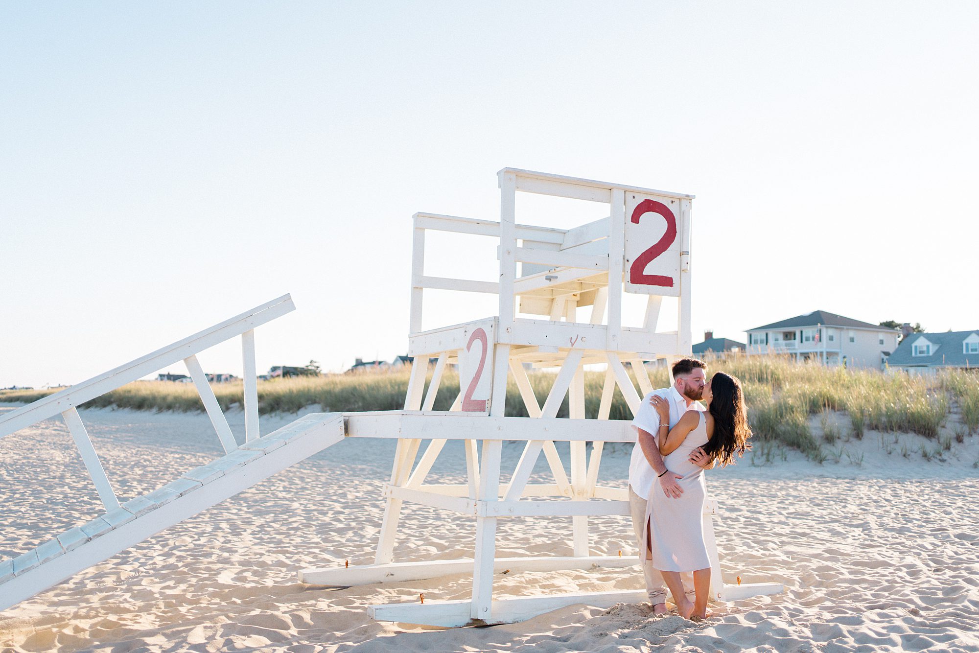 engaged couple kiss by lifeguard stand at Jersey shore