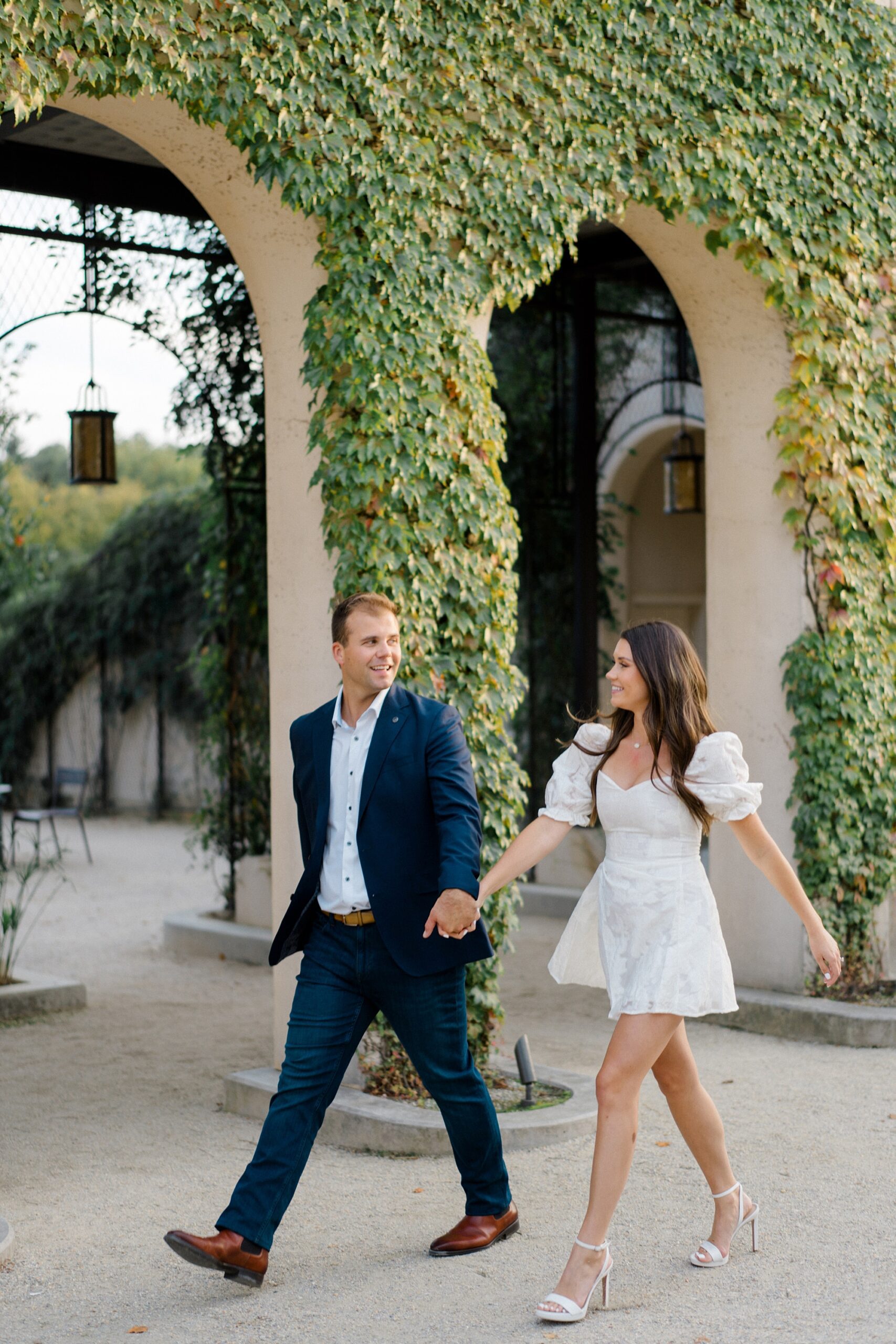 engaged couple walk by building covered in vines at Longwood Gardens 