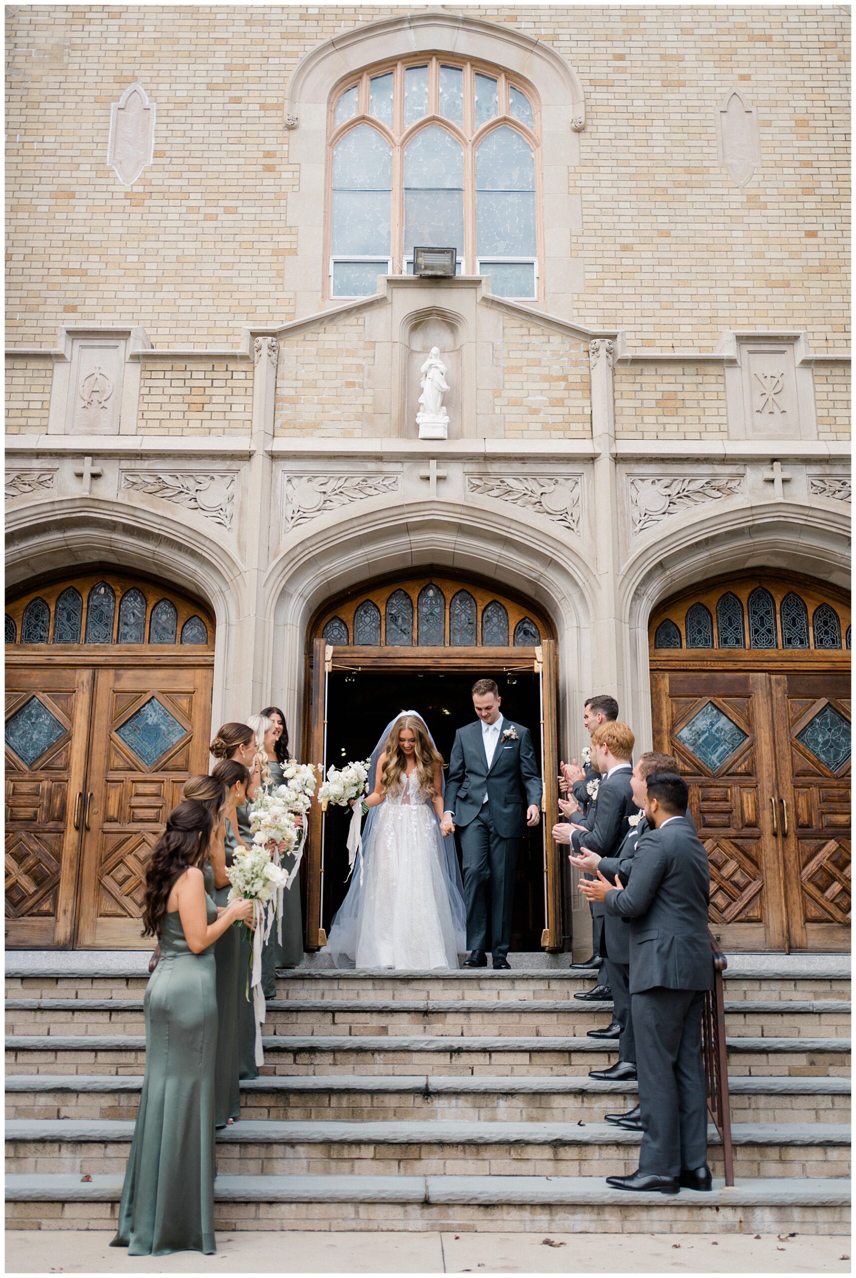 newlyweds walk out of church as wedding party line the stairs
