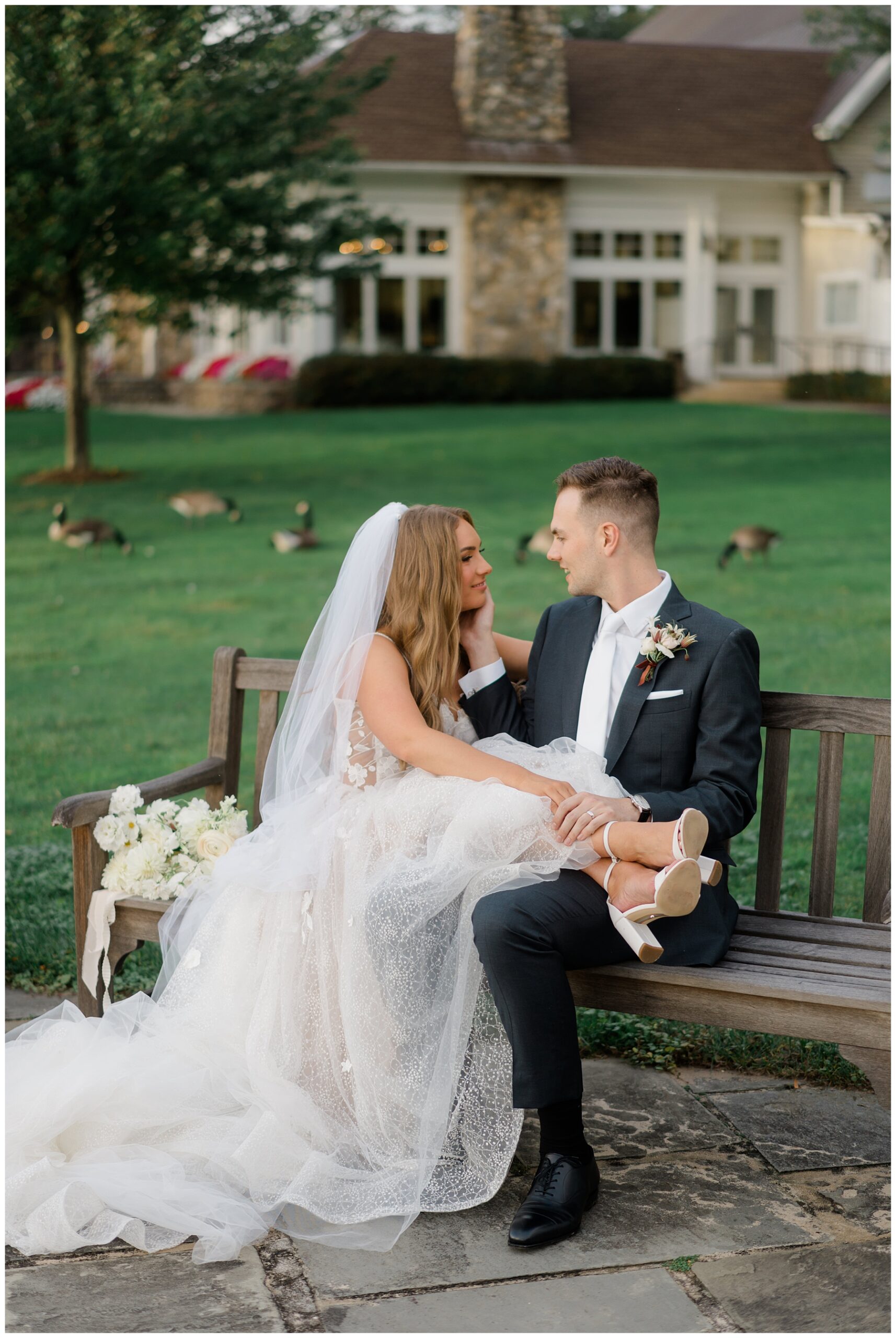 newlyweds sit on bench by lake at Indian Trail Club Wedding