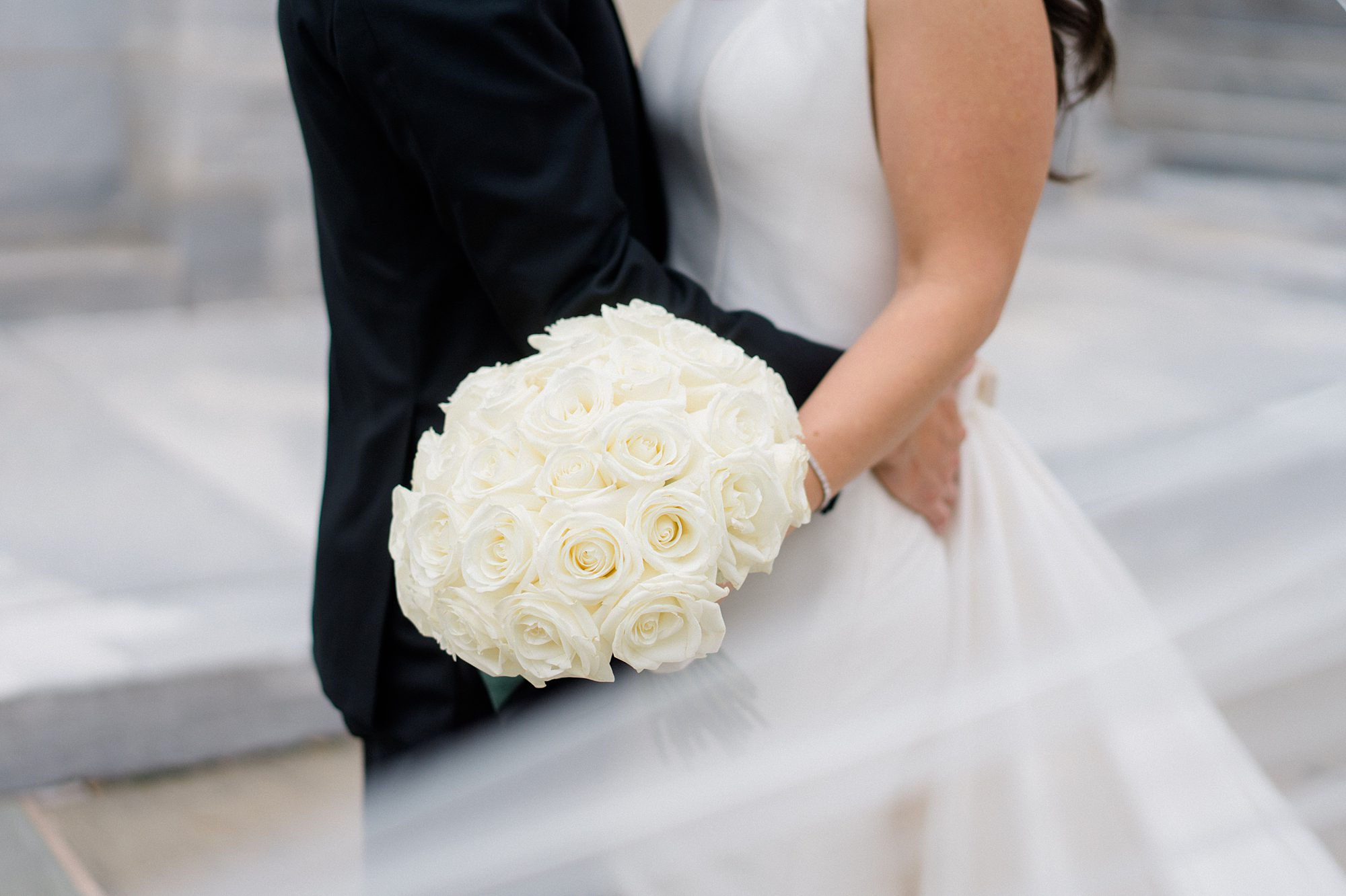 bride and groom hug and bride holds white rose bouquet