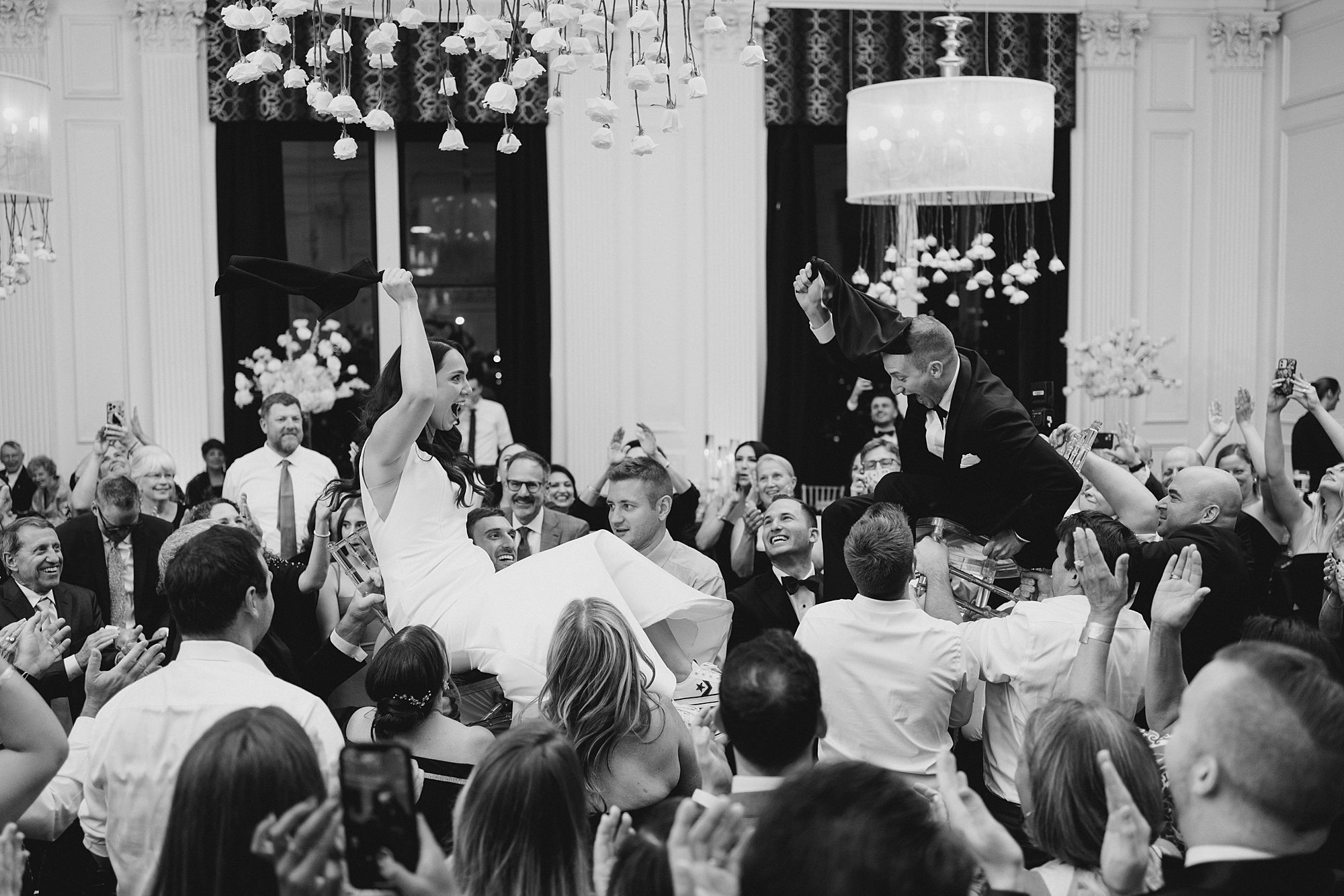 guests lift the bride and groom up on chairs during Chic Down Town Club Wedding reception
