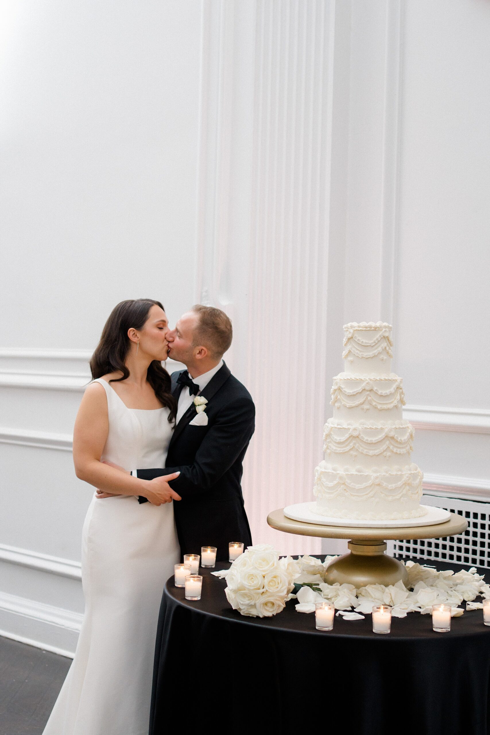 bride and groom kiss by their classic wedding cake