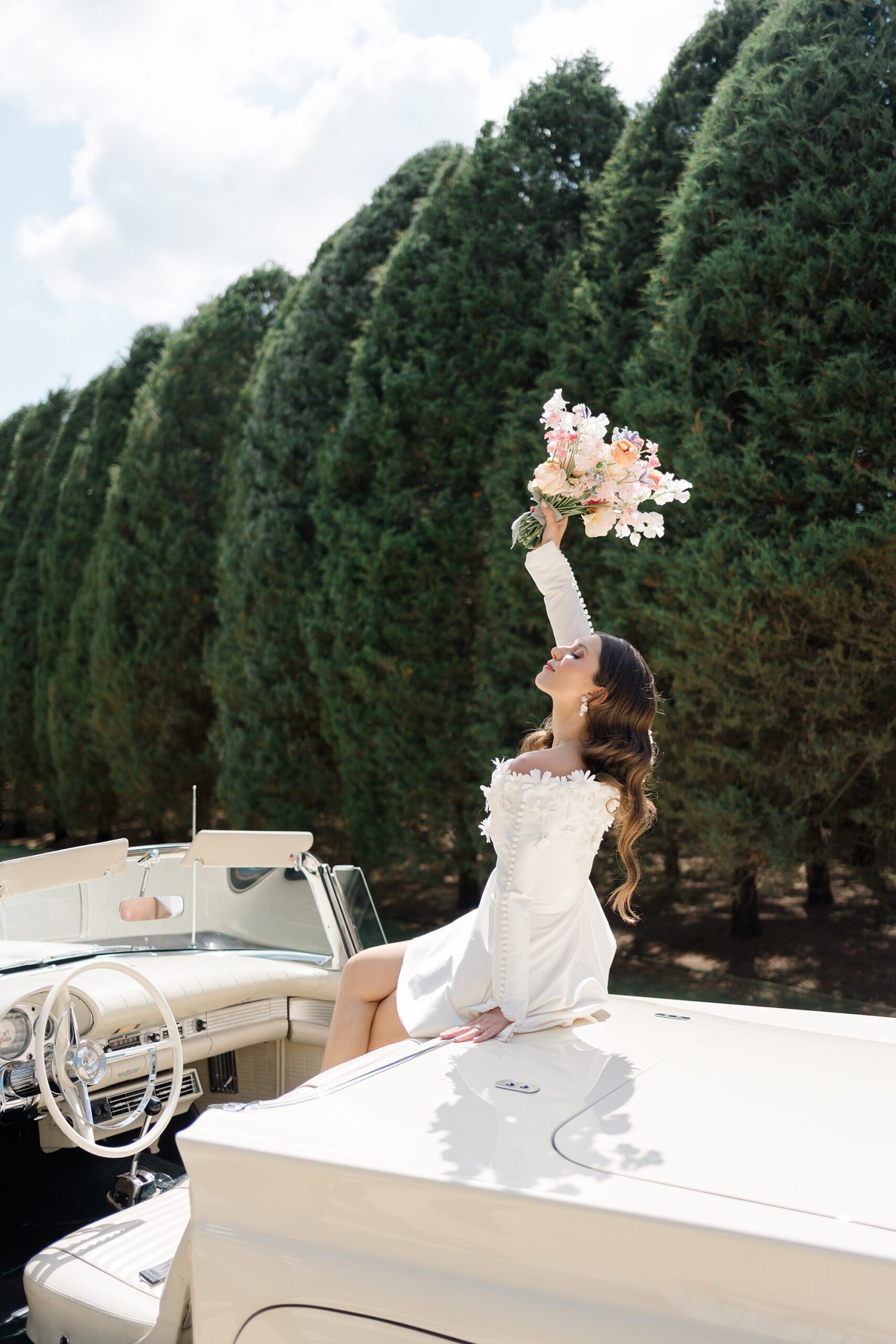 bride sits in classic car holding up bridal bouquet
