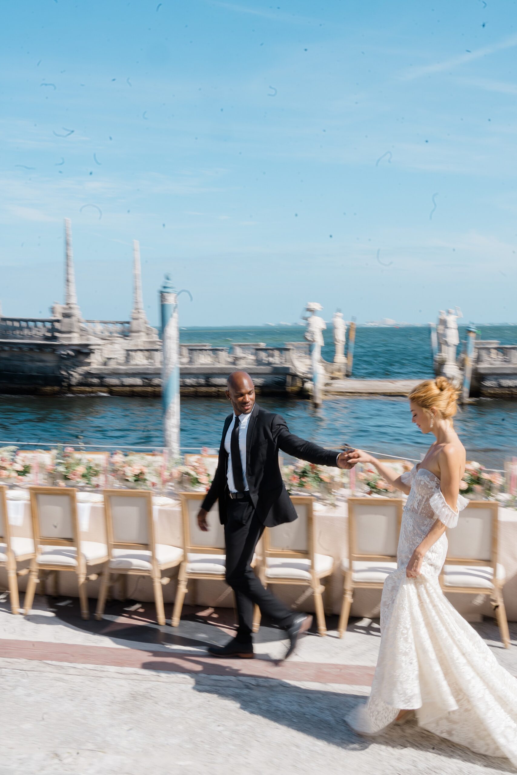 newlyweds walk by table at outdoor reception 