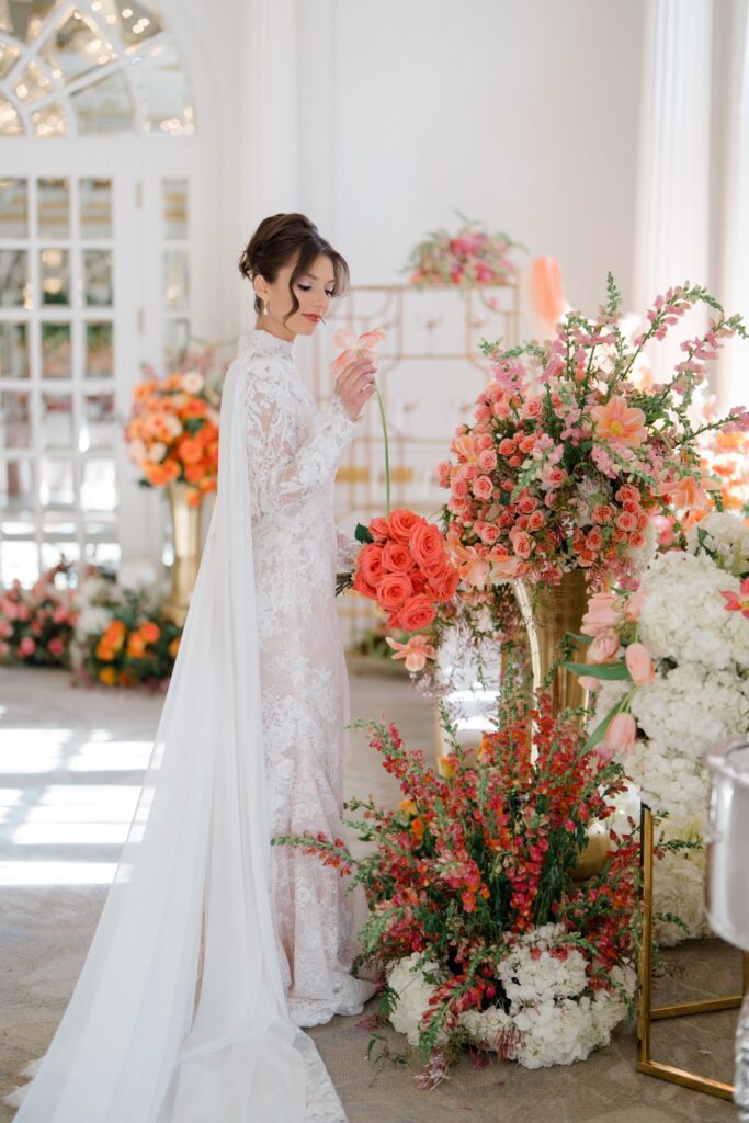bride in lace dress admiring a light orange flower during styled shoot at Crystal Plaza