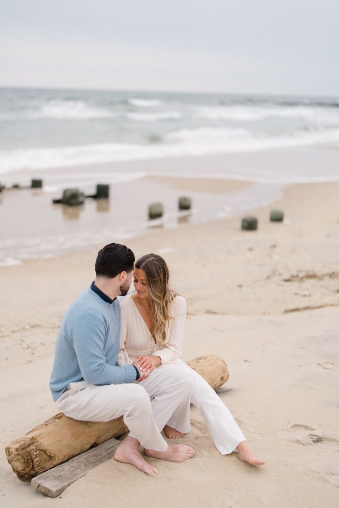 Couple sitting on a log on the beach during Spring Lake Engagement